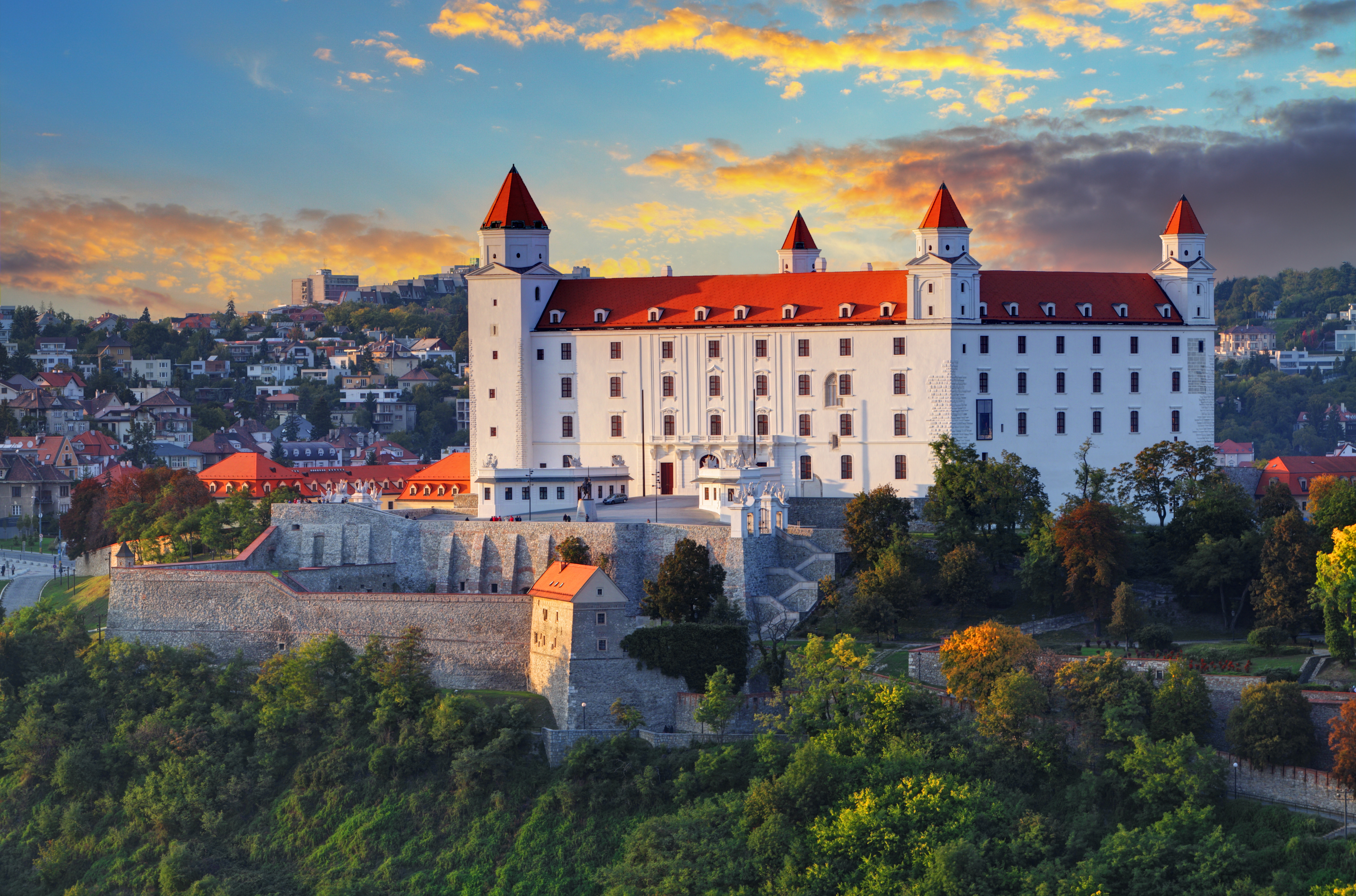 Det historiske hvide Bratislava-slot med fire tårne oplyst ved solnedgang med udsigt over Donau-floden og byens skyline i Slovakiet