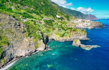 Betagende luftfoto af Bridal Veil vandfaldet (Veu da Noiva) der falder fra grønne klipper ved Ponta do Poiso på Madeiras vilde atlanterhavskyst