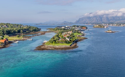 Luftfoto af Brønnøysund kysten i Norge med små øer, traditionelle huse og blåt vand omgivet af bjerge i Helgeland regionen
