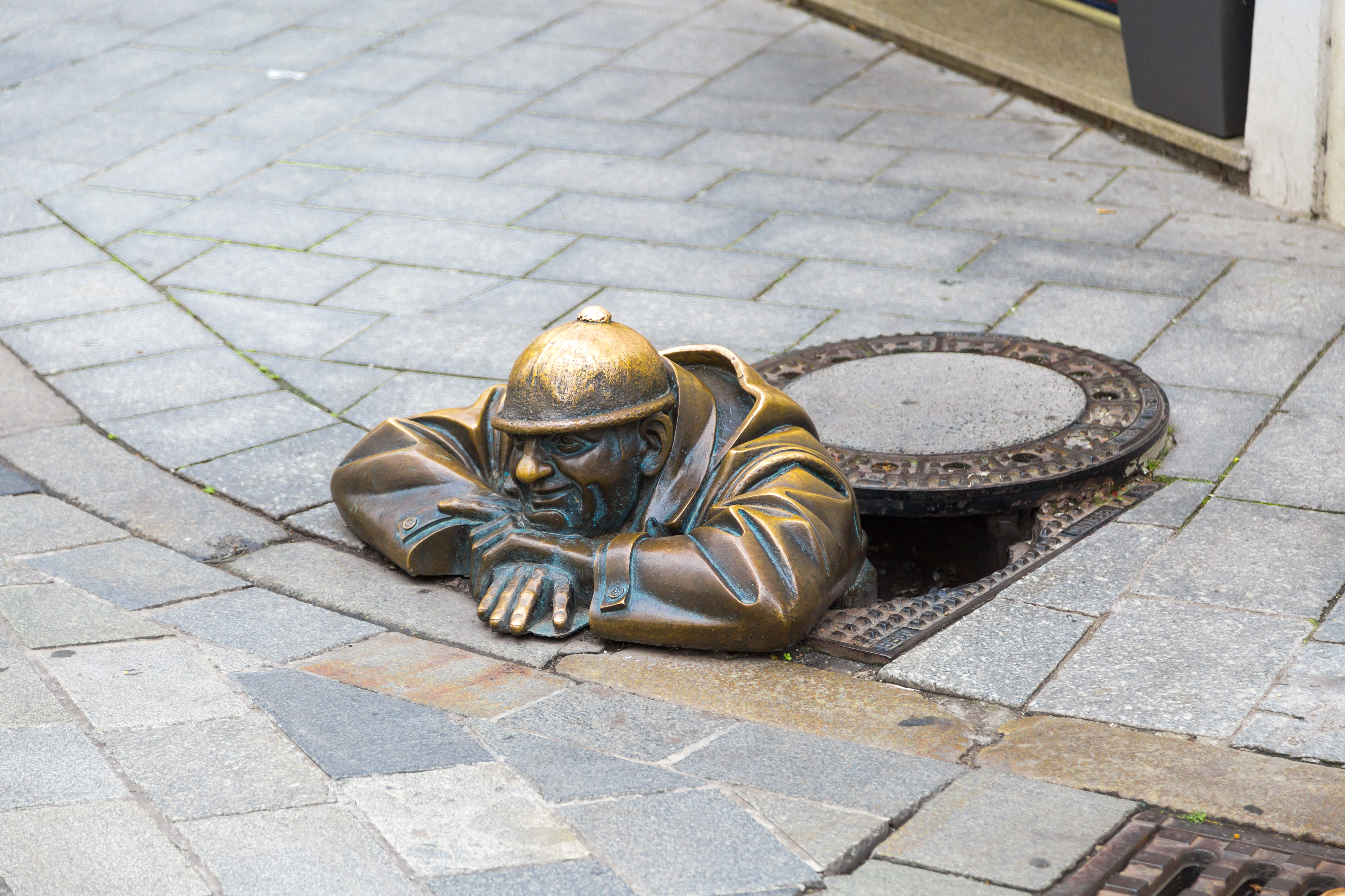 Bronze statue af mand der kravler op fra kloakdæksel på brostensstrøg i Bratislava Slovakiet