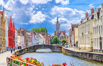 Idyllisk udsigt over Spiegelrei-kanalen i Brugge med den ikoniske Poortersloge-tårn, Kongebroen og farverige middelalderlige bygninger langs bredden i Belgiens smukkeste historiske bycentrum