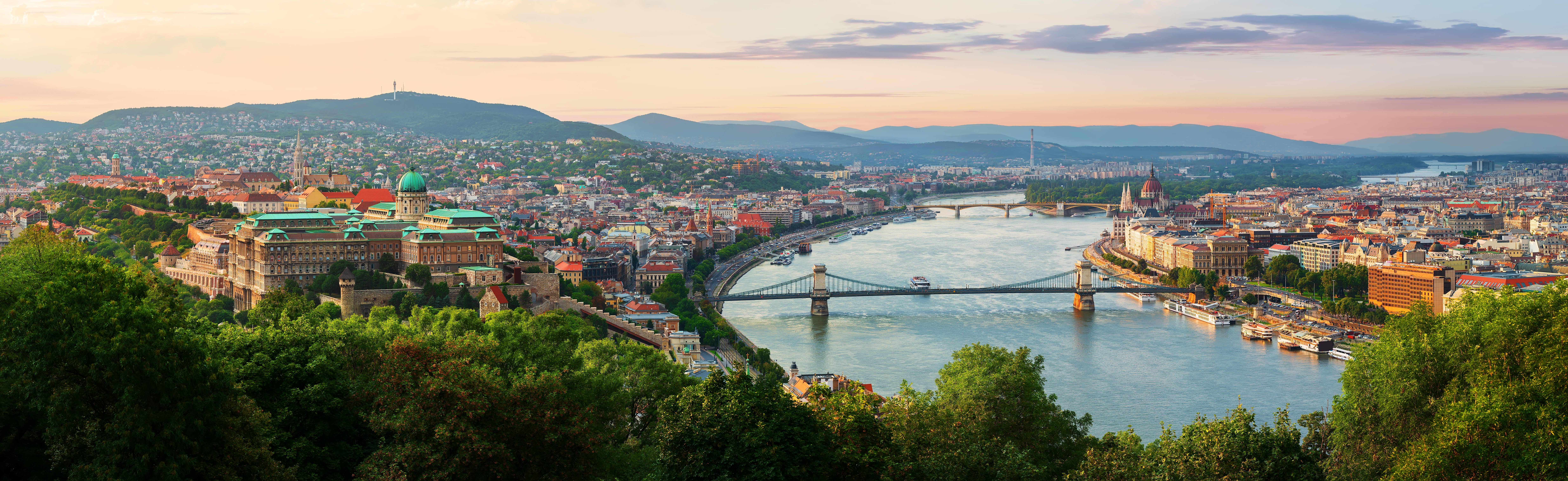 Panoramaudsigt over Budapest med Donau-floden, Kædebroen og Buda-bjergene ved solnedgang