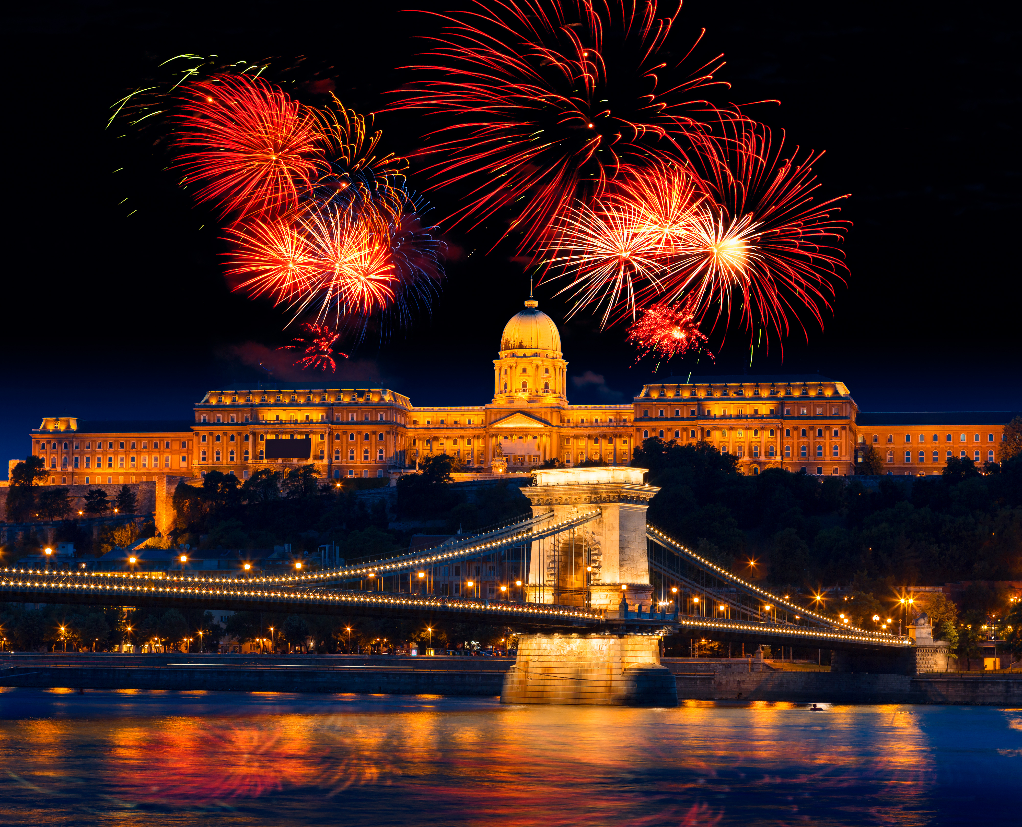 Farverigt nytårsfyrværkeri over Budapest med oplyst Budaborg og Kædebroen spejlet i Donau-floden, Ungarn