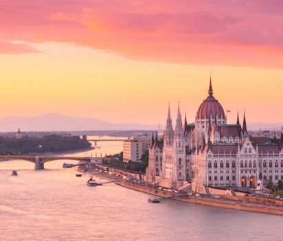 Betagende solnedgang over Budapest med den ikoniske ungarske parlamentsbygning og Donaufloden, hvor Margaretbroen forbinder Buda og Pest i det gyldne aftenlys
