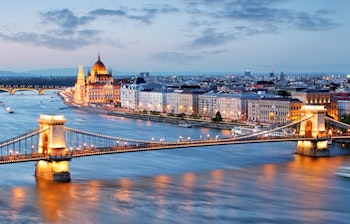 Betagende panoramaudsigt over Budapests skyline ved solnedgang med det oplyste parlamentsbygning, Széchenyi-kædebroen og Donaufloden, der viser Ungarns historiske hovedstad