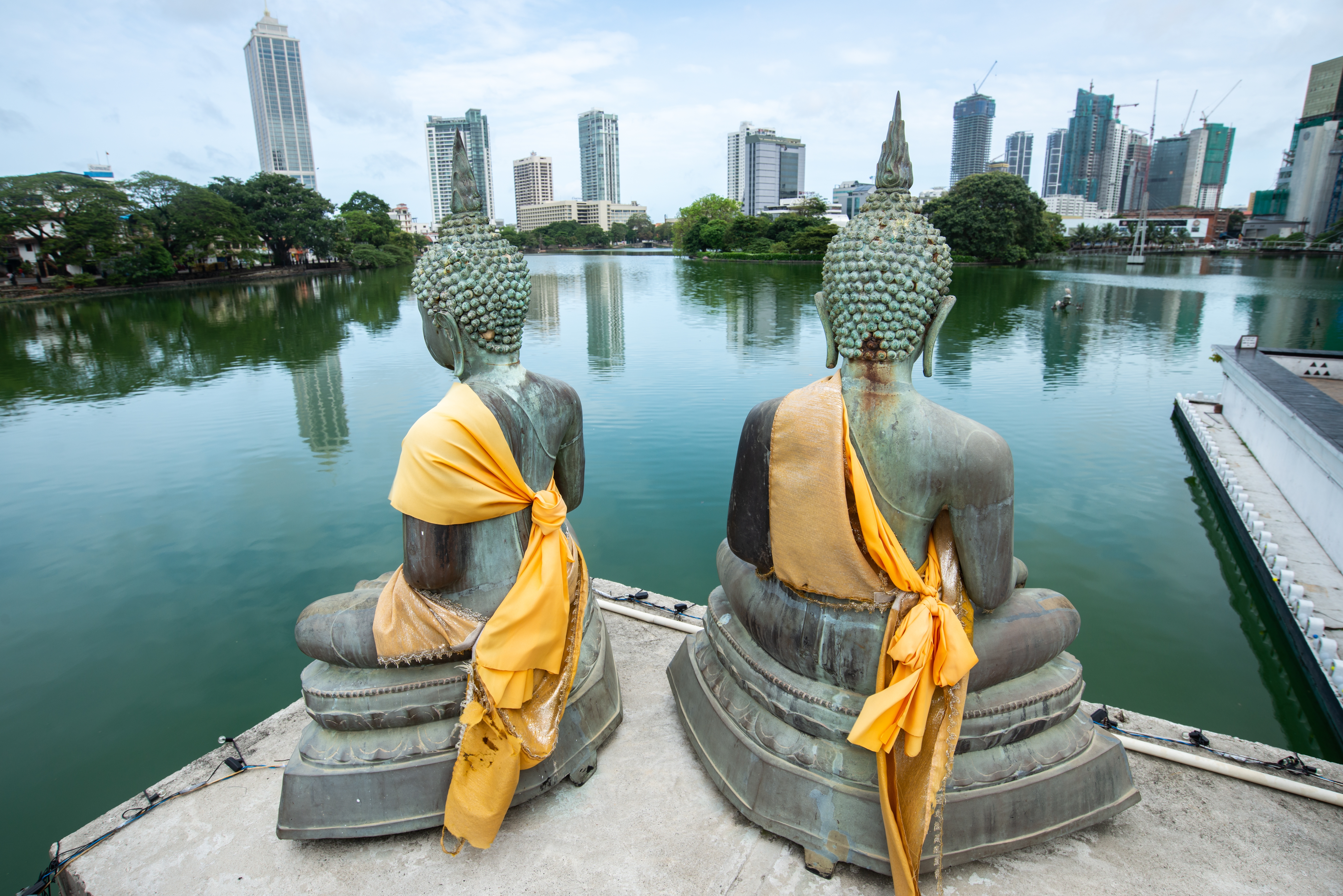 To Buddha-statuer i gylden kjortel med udsigt over Colombos skyline og sø i Sri Lanka