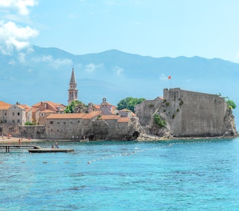 Historiske Budva i Montenegro med den gamle bydel, kirketårn og fæstning omgivet af det azurblå Adriaterhav og bjergkæde i baggrunden