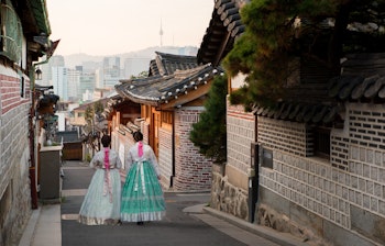 To kvinder iført farverige traditionelle koreanske hanbok-dragter spadserer gennem den historiske Bukchon Hanok-landsby i Seoul, Sydkorea - en kulturel oplevelse blandt traditionelle træhuse