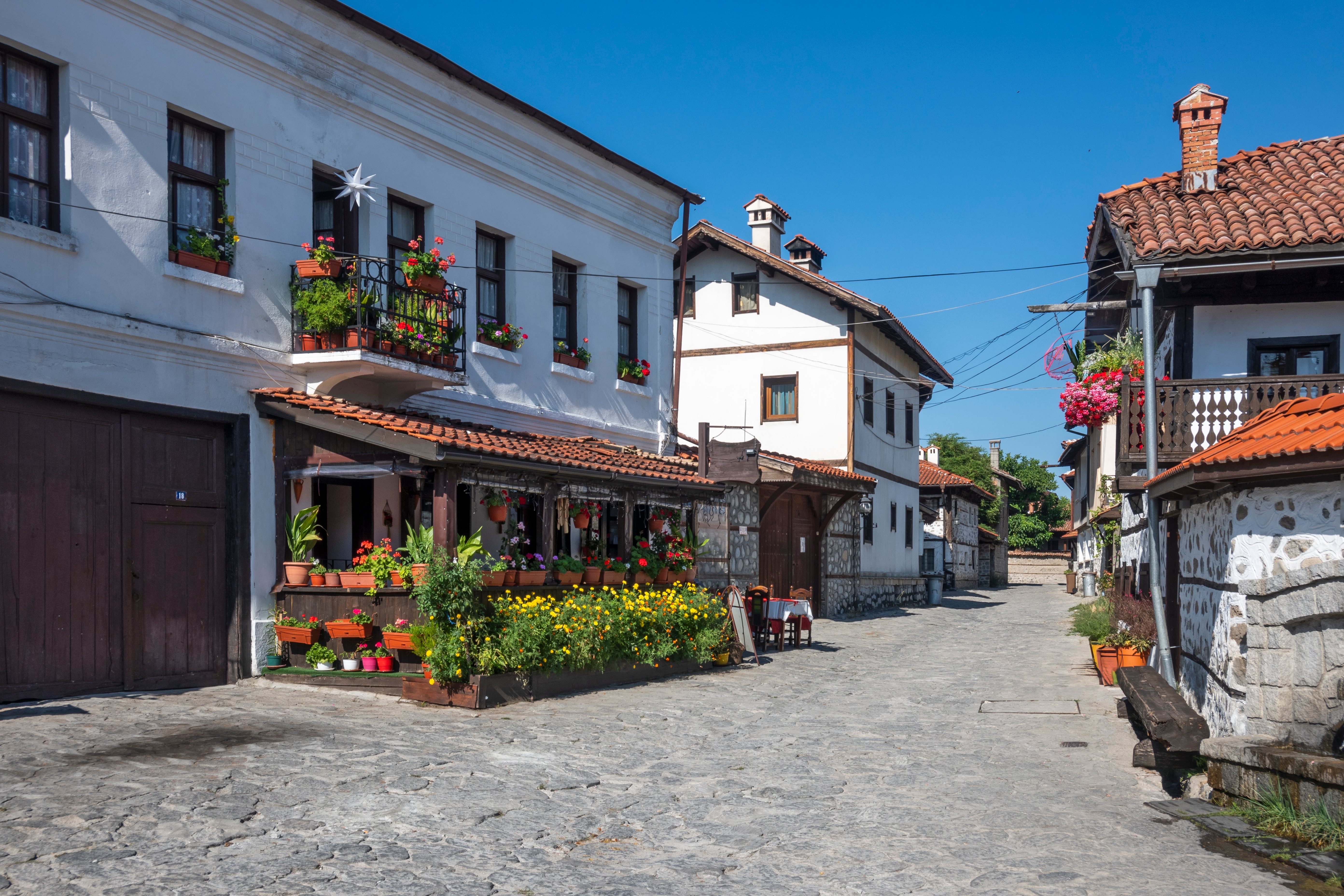 Pittoresk brolagt gade i historisk bulgarsk bjerglandsby med traditionelle hvide huse og røde tegltage