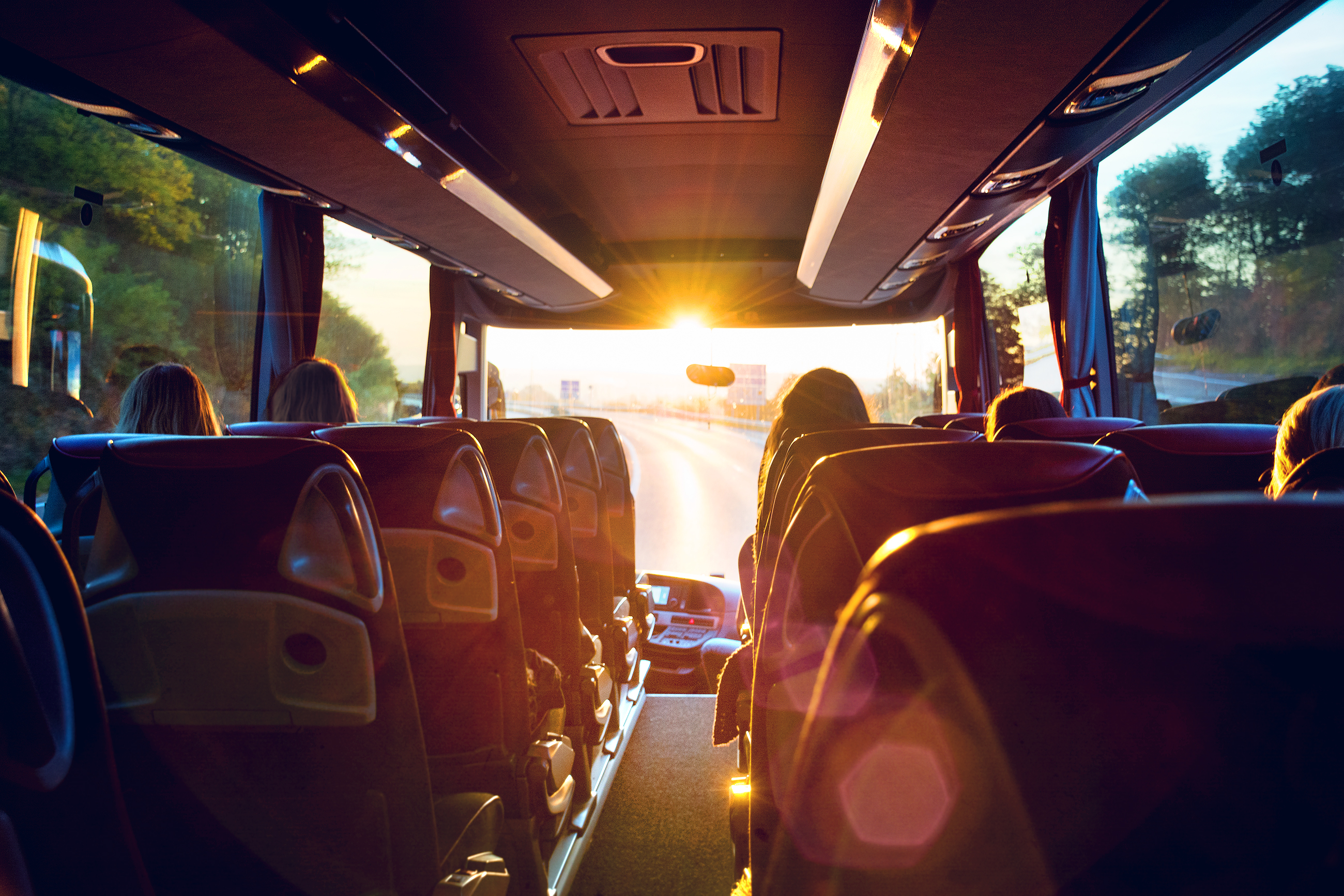 Passagerer på luksus turistbus under rejse med solnedgang gennem vinduerne