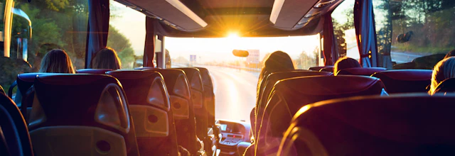 Passagerer på luksus turistbus under rejse med solnedgang gennem vinduerne