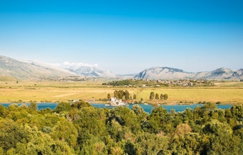 Panoramaudsigt over Vivari-kanalen med blåt vand, grøn vegetation og bjerge i UNESCO-beskyttede Butrint Nationalpark i Albanien