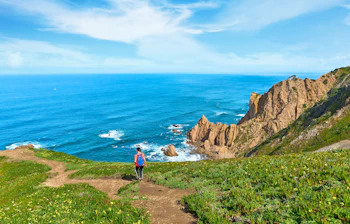 Kvinde på vandretur langs de imponerende klipper ved Cabo da Roca i Portugal, med udsigt over Atlanterhavets blå vand og dramatiske kystlinje