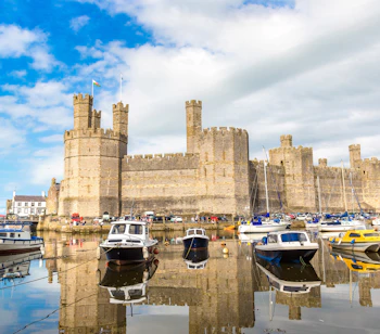 Historiske Caernarfon Slot med middelalderlige taarne og baade i havnen i Nordwales