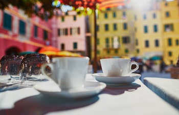 Kaffekopper på udendørs cafébord med farverige bygninger i Vernazza, Cinque Terre - idyllisk italiensk ferieoplevelse