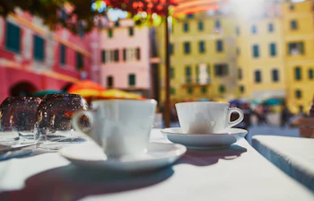 Kaffekopper på udendørs cafébord med farverige bygninger i Vernazza, Cinque Terre - idyllisk italiensk ferieoplevelse