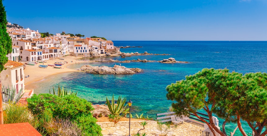 Idyllisk fiskerby Calella de Palafrugell ved Costa Brava med hvide bygninger langs sandstranden og det turkisblå Middelhav i Catalonien, Spanien