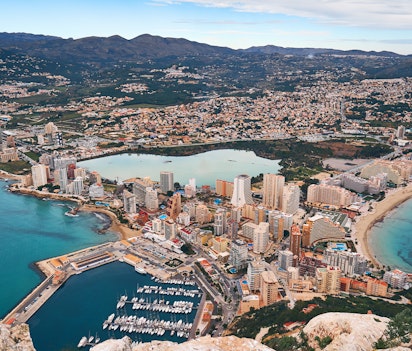 Spektakulært dronefoto af Calpe med den ikoniske Penon de Ifach-klippe, saltsøen og det azurblå Middelhav på begge sider, der viser byens unikke kystlandskab på Costa Blanca