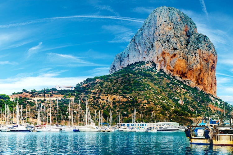 Betagende solnedgang over stranden i Calpe med den majestætiske Penon de Ifach-klippe, Middelhavets azurblå vand og kystbyens charmerende panorama i Alicante, Spanien