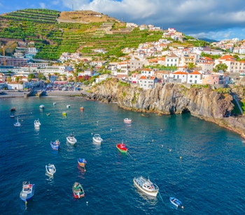 Luftfoto af den farverige fiskerby Câmara de Lobos på Madeira med både i bugten og maleriske huse på bakkerne