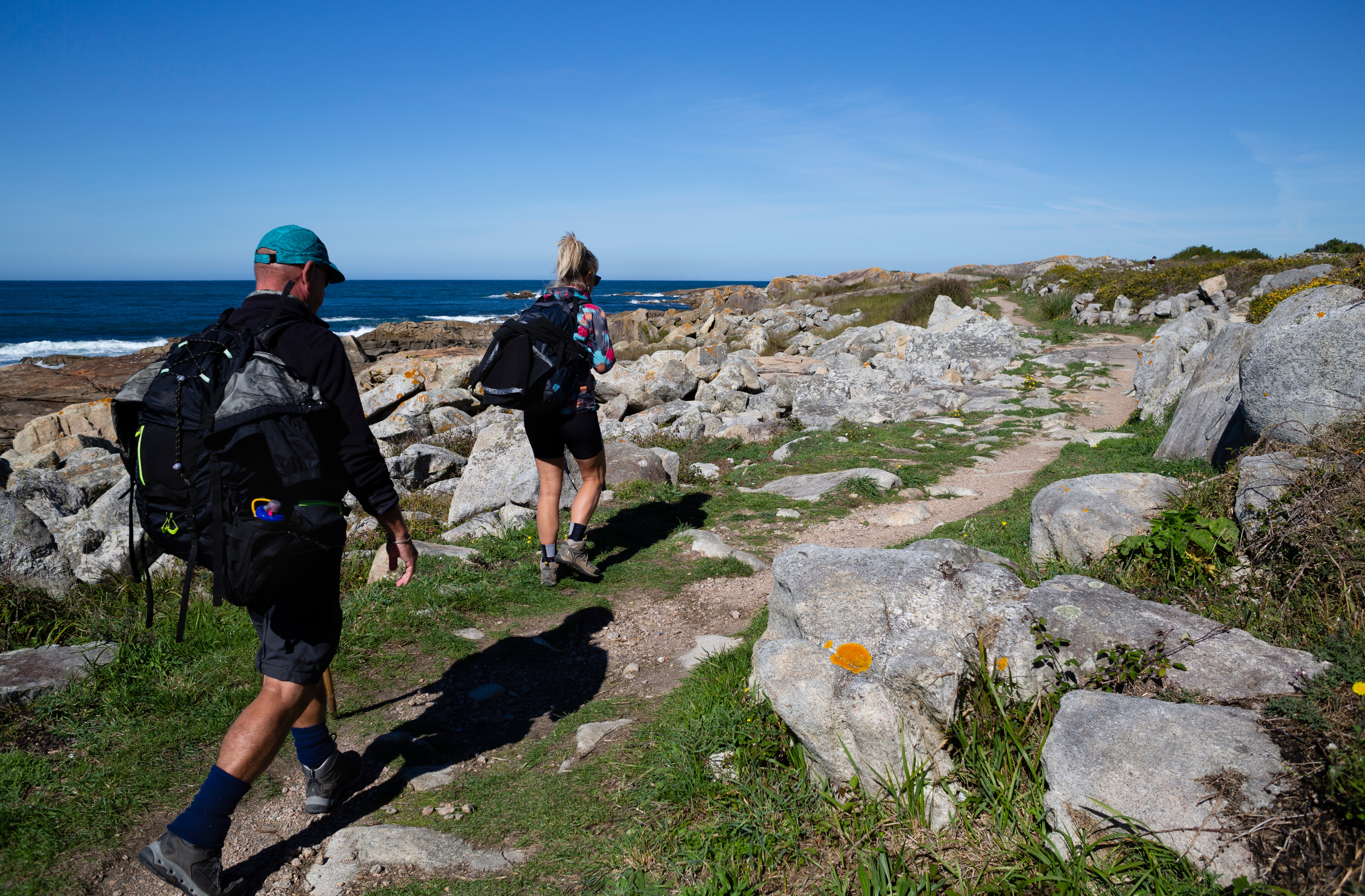 To pilgrimme vandrer den portugisiske Camino de Santiago langs kysten ved A Guarda i Galicien med rygsække og blå hav i baggrunden
