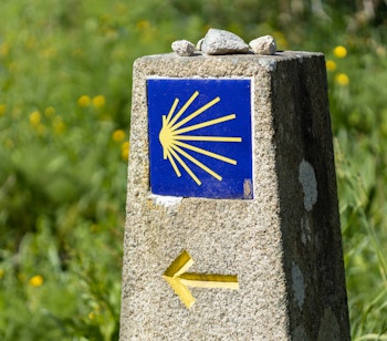 Karakteristisk stenvejviser på Caminoen med gul muslingeskal og retningspil, der guider pilgrimme mod Santiago de Compostela i Spanien