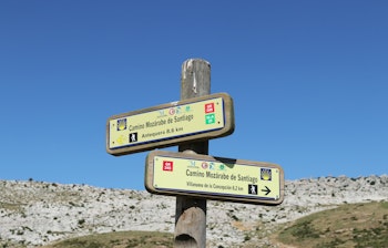 Træskilt på Camino Mozarabe pilgrimsruten i Andalusien, Spanien, der viser vej mod Santiago de Compostela under en klar blå himmel
