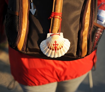 Traditionel hvid Jakobsmusling fastgjort til en rød rygsæk tilhørende en pilgrim på vandring langs Caminoen i Spanien, symboliserende den historiske pilgrimsrejse