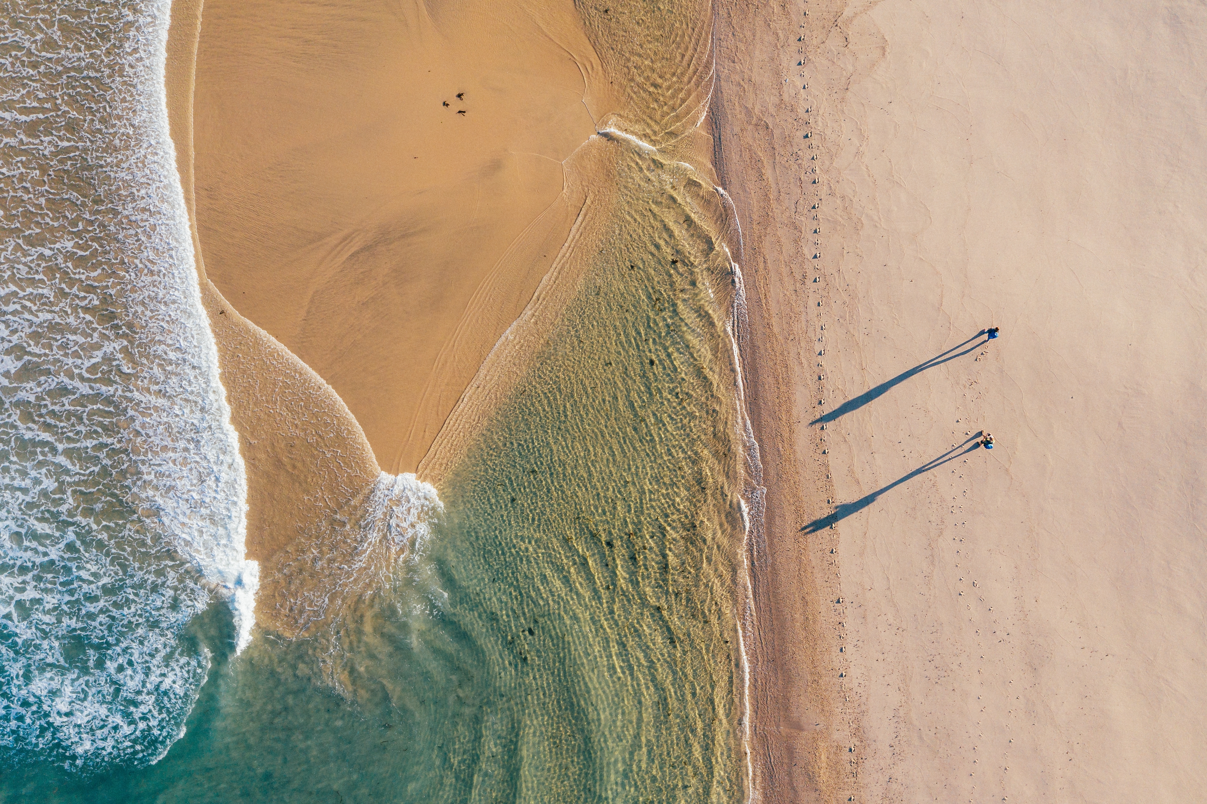 Luftfoto af et par der vandrer langs en smuk sandstrand ved Atlanterhavet under solopgang på Camino Portugués ruten, med lange skygger på sandet