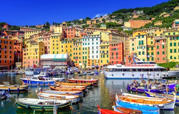 Maleriske pastellfarvede huse langs havnefronten i den historiske fiskerby Camogli med traditionel italiensk arkitektur og både i vandet nær Genova