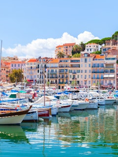 Idyllisk udsigt over Cannes marina på den franske riviera med luksuriøse yachter og farverige bygninger under blå sommerhimmel