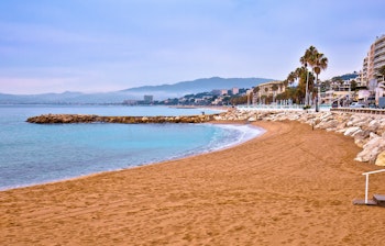 Panoramaudsigt over Cannes' sandstrand med palmer langs vandkanten, populær feriedestination på den franske riviera