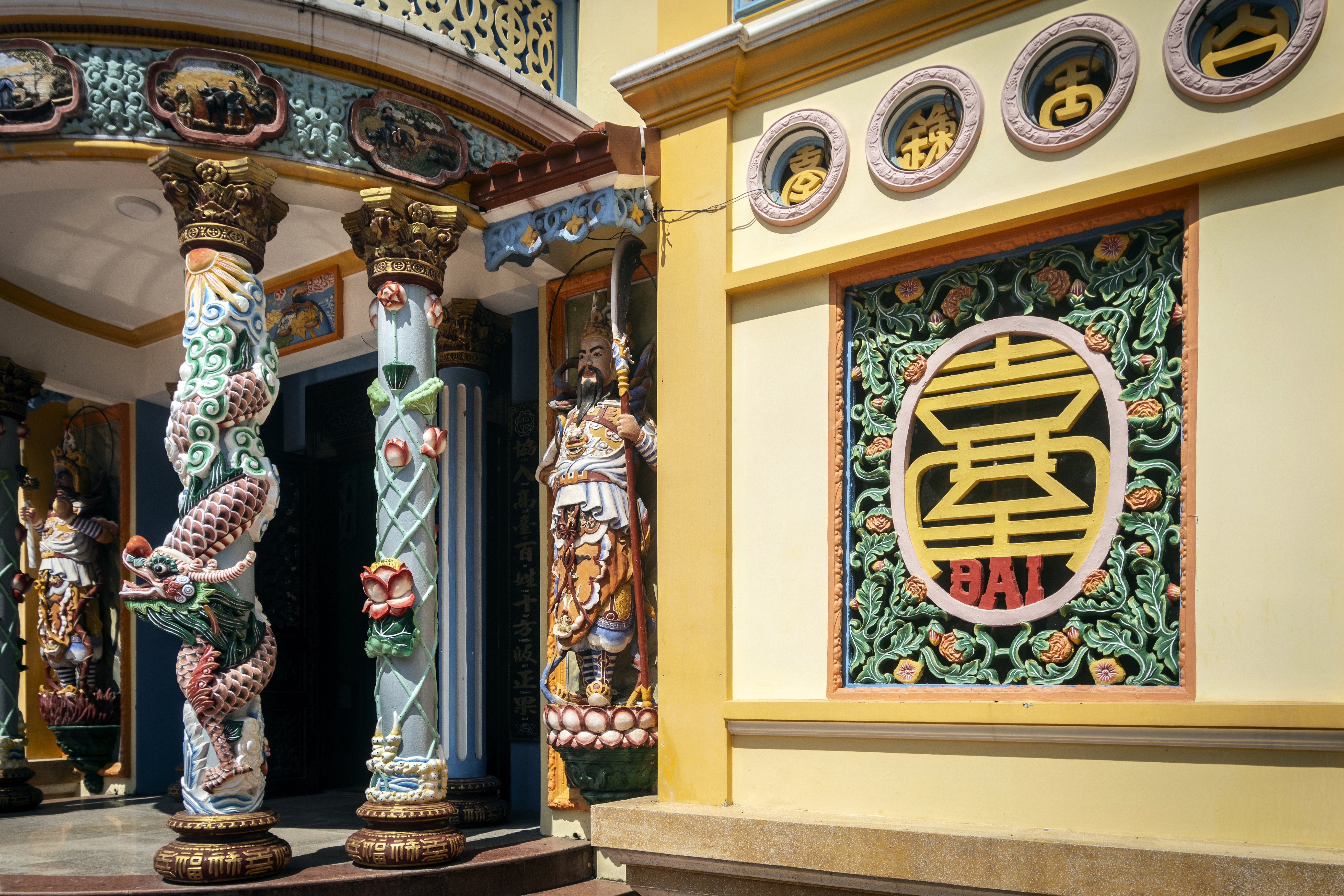 Farverig Cao Dai tempel facade i Hoi An, Vietnam, med detaljerede dragesøjler og traditionel vietnamesisk religiøs arkitektur