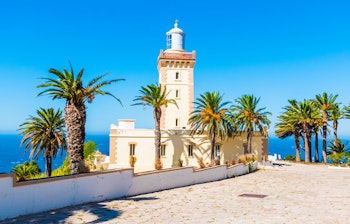 Det historiske Cap Spartel-fyrtårn nær Tanger i Marokko, hvor Middelhavet møder Atlanterhavet med palmer i forgrunden