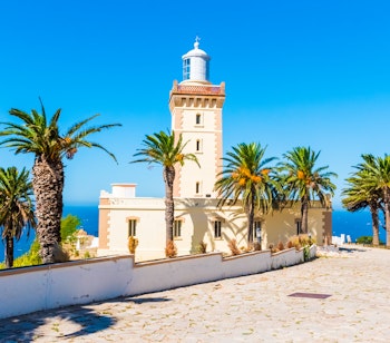 Det historiske Cap Spartel-fyrtårn nær Tanger i Marokko, hvor Middelhavet møder Atlanterhavet med palmer i forgrunden