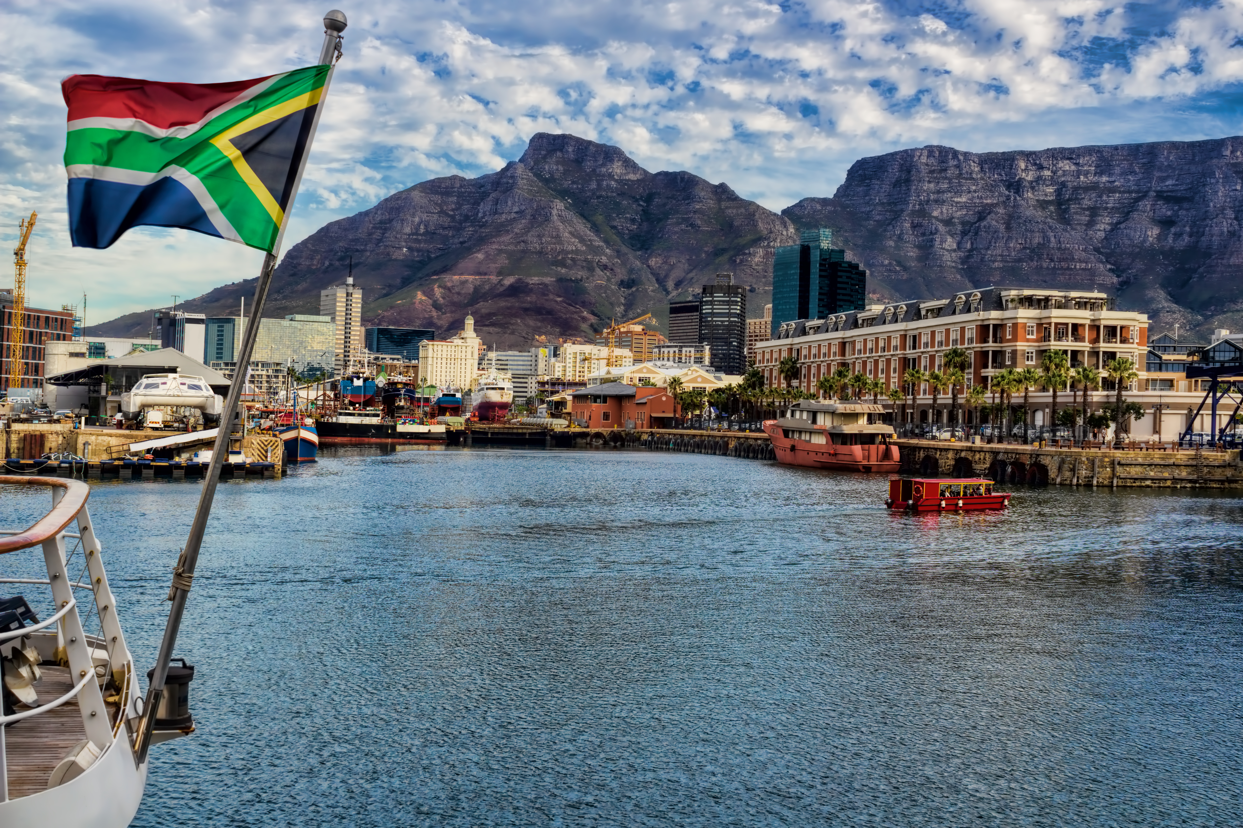 Cape Town havn med Table Mountain i baggrunden og sydafrikansk flag på båd