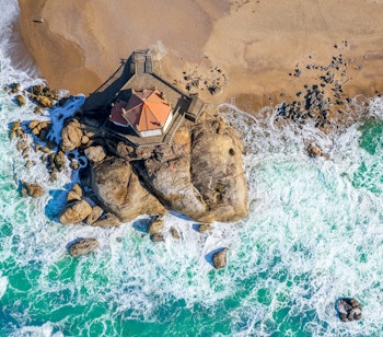 Luftfoto af det historiske kapel Capela do Senhor da Pedra bygget på klipper i Atlanterhavet ved Miramar-stranden syd for Porto