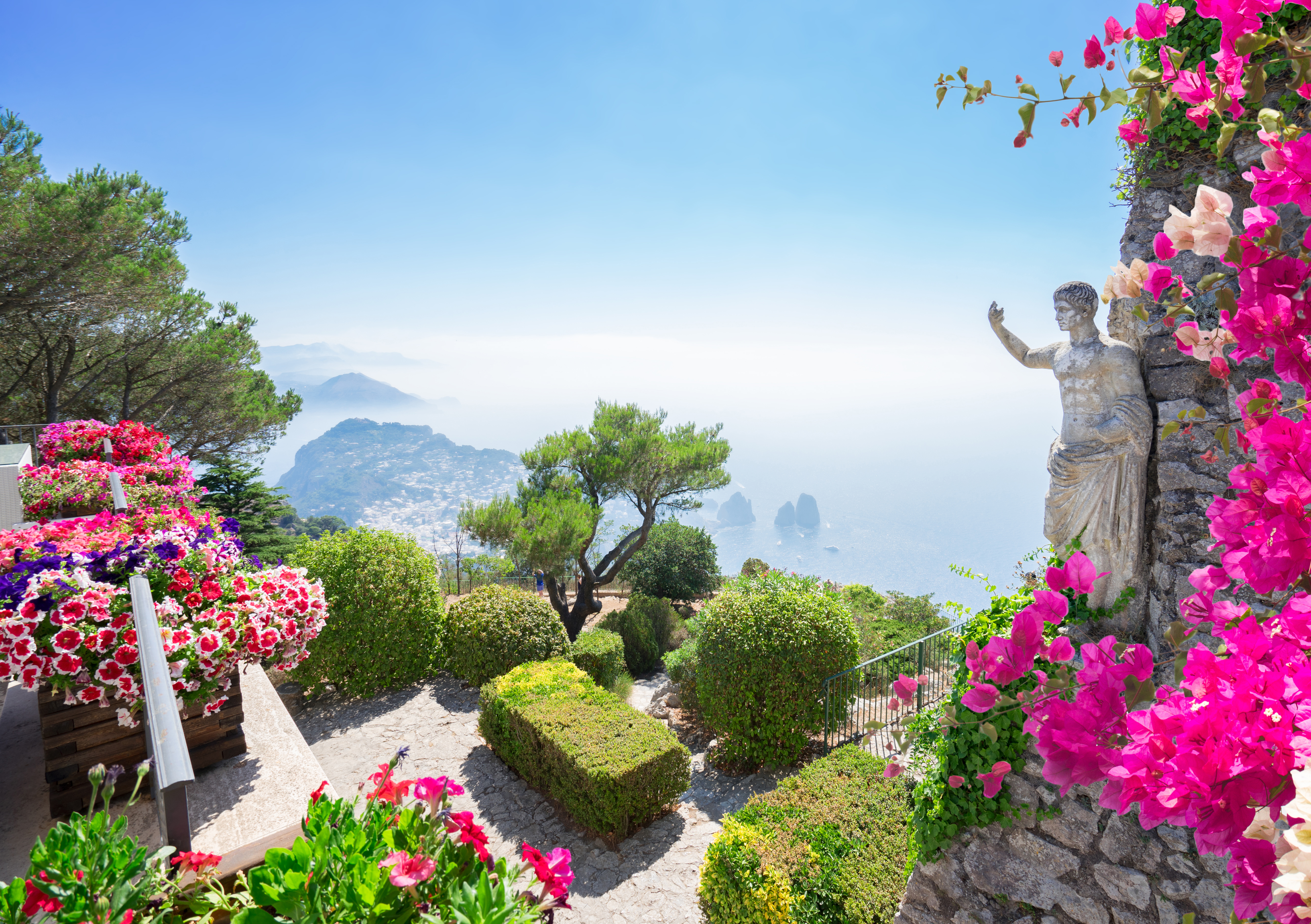 Smuk haveterrasse med statue og lyserøde blomster med udsigt over Middelhavet og Capris kystlinje