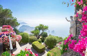 Smuk haveterrasse med statue og lyserøde blomster med udsigt over Middelhavet og Capris kystlinje