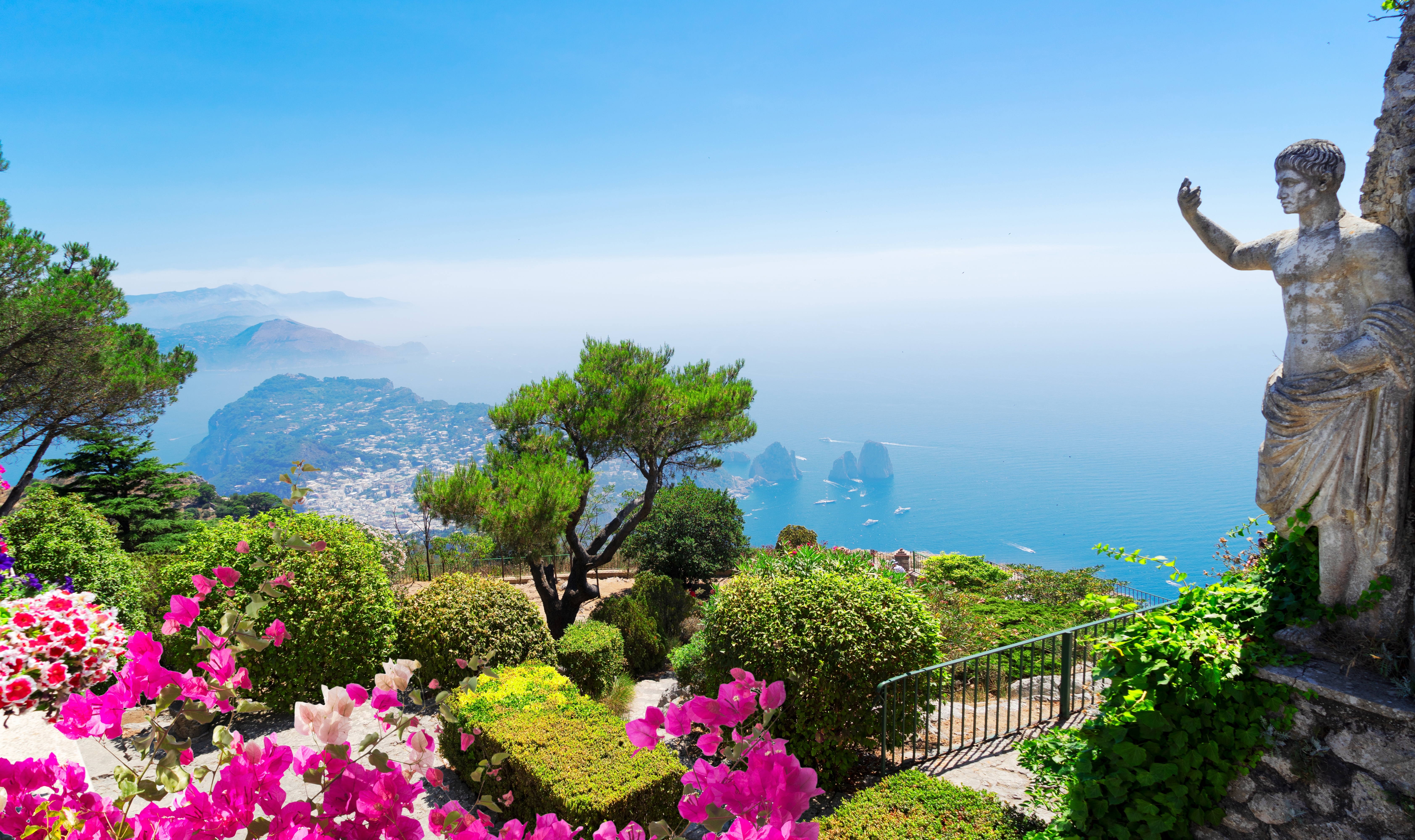 Fantastisk panoramaudsigt over Capri med klassisk statue og farverige blomster med udsigt over Middelhavet