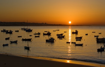 Fredelig morgenstemning med fiskerbåde fortøjet i Cascais havn ved solopgang, Portugal, med gyldent lys reflekteret i det stille vand