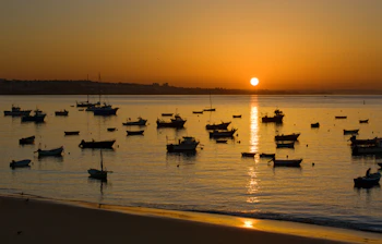 Fredelig morgenstemning med fiskerbåde fortøjet i Cascais havn ved solopgang, Portugal, med gyldent lys reflekteret i det stille vand