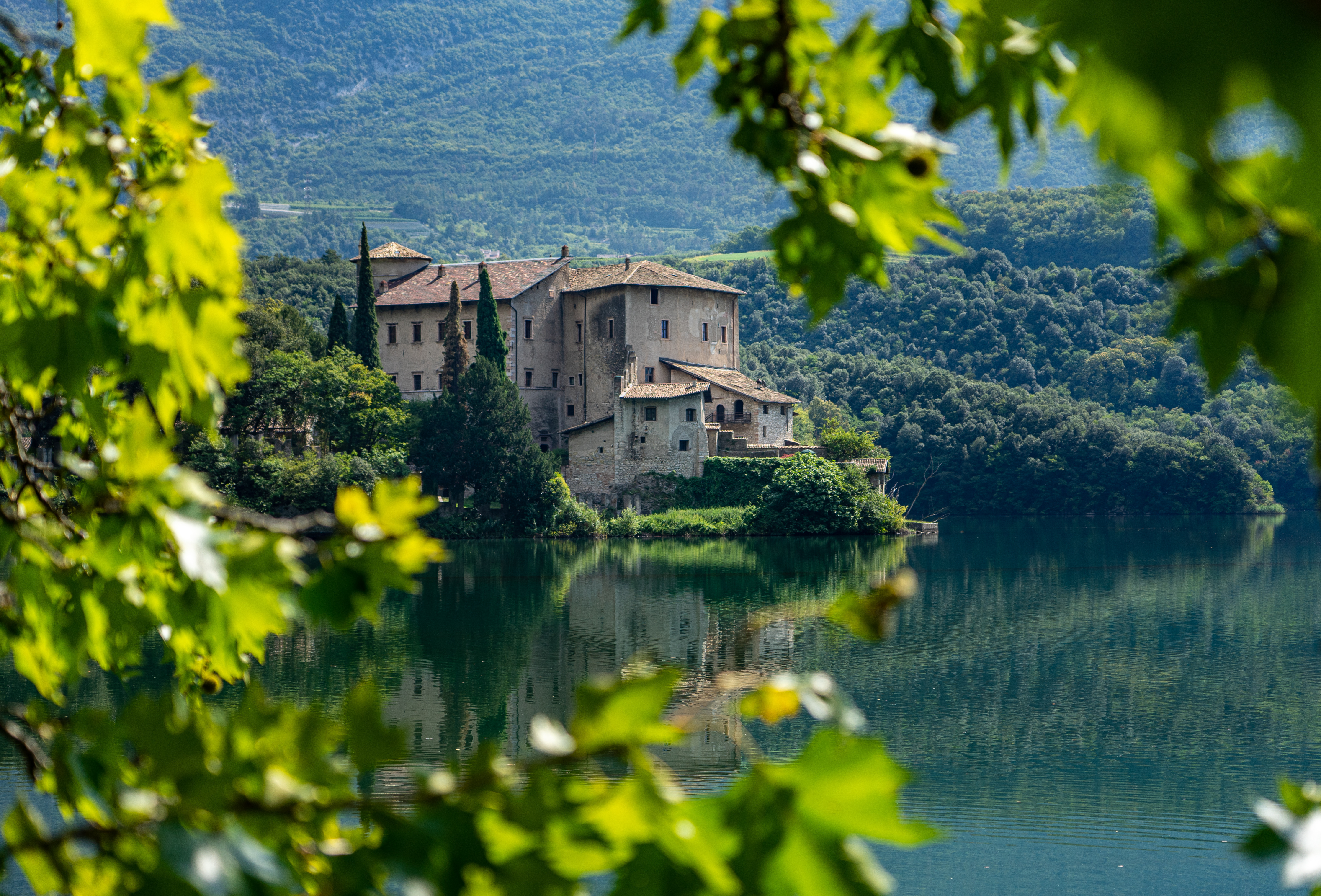 Det middelalderlige Castel Toblino slot spejler sig i det rolige Toblino-søs vand omgivet af grønne skove i Trentino, Italien