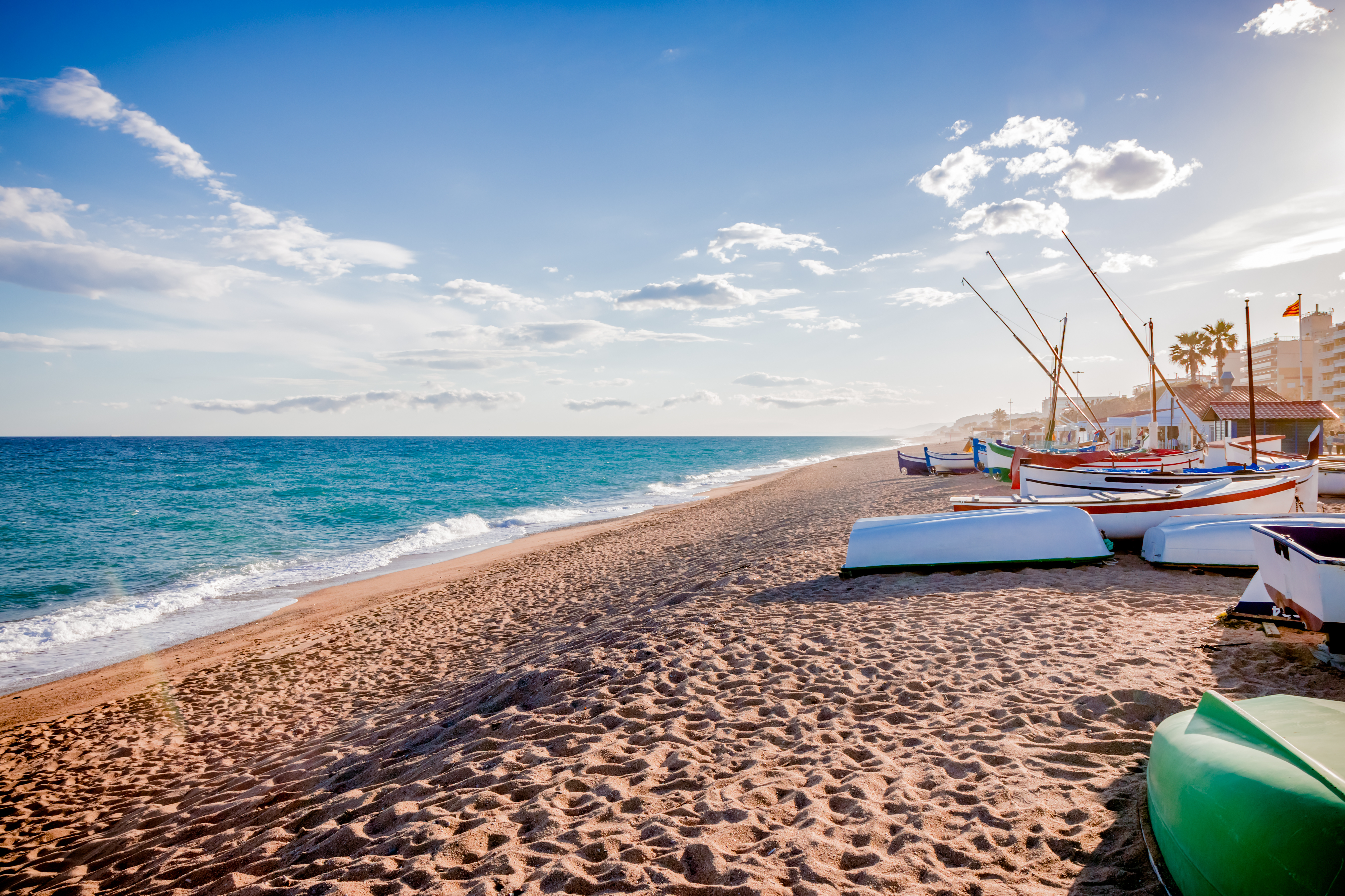 Traditionelle catalanske fiskerbåde på en sandstrand ved Middelhavet i Catalonien, Spanien, med turkisblåt vand og blå himmel