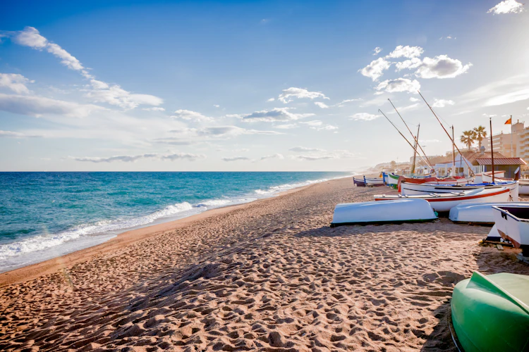 Traditionelle catalanske fiskerbåde på en sandstrand ved Middelhavet i Catalonien, Spanien, med turkisblåt vand og blå himmel