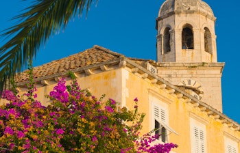 Idyllisk udsigt over Cavtat by med traditionel arkitektur, gule blomster og tårn under klar blå himmel på Dubrovnik Riviera, Kroatien