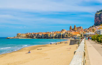 Betagende udsigt over den historiske kystby Cefalù på Sicilien med dens maleriske bygninger, katedral og gyldne strand ved Middelhavets azurblå vand