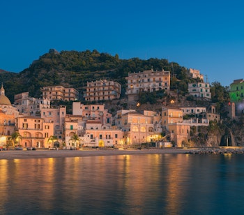 Solnedgang over det farverige fiskerleje Cetara på Amalfikysten med traditionelle bygninger oplyst langs Middelhavets kystlinje