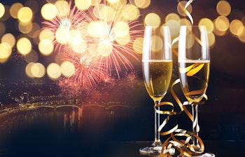 Champagne glas med gylden fyrværkeri og funklende bylys til nytårsfejring