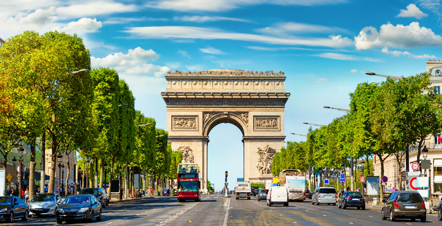 Den berømte Champs-Élysées boulevard i Paris med træer langs siderne, der fører til den majestætiske Triumfbue under klar blå himmel - Frankrigs mest eksklusive shoppinggade